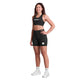 En kvinde smiler iført Saysky Zig Zag Combat Sports Bra, Dame, Black Zigzag og matchende højtaljede shorts lavet af genanvendt Combat-materiale, plus hvide sokker og sneakers - ideelt til løb med høj intensitet.