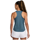 En kvinde med langt krøllet hår i en hestehale kigger væk, iført en Nike Dri-Fit Running Tank Top for dame i Smokey Blue/Reflective Silver og hvide shorts på en almindelig hvid baggrund.