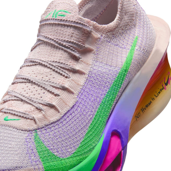 Et nærbillede af en beige strik-sneaker med en grøn Nike-swoosh, farverig lilla og orange gradueret mellemsål og sætningen "No Human is Limited" skrevet på siden af sålen.
