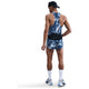En mand kigger væk iført en Nike Aeroswift Singlet, Herre, Coastal Blue/White løbevest og shorts, hvide sokker, løbesko, en sort bæltetaske og en sort bagudvendt kasket på en hvid baggrund.