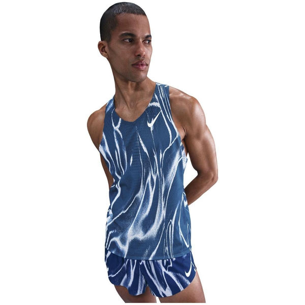 En person iført Nike Aeroswift Singlet, Herre i Coastal Blue/White står med armene bag ryggen og kigger til siden mod en almindelig hvid baggrund.