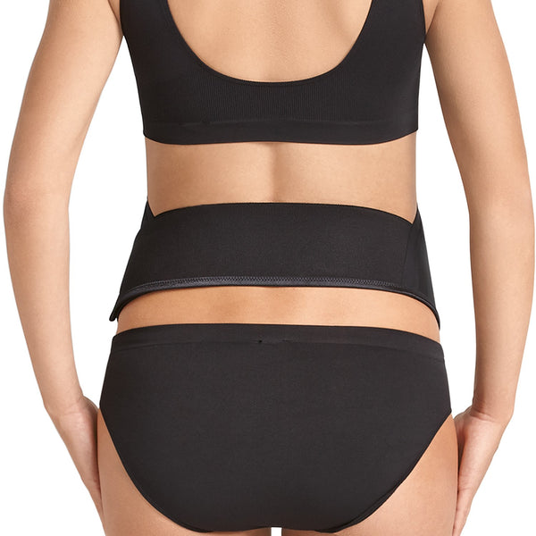 En person iført sort undertøj ses bagfra med Anita BabyBelt til kvinder i sort spændt fast om maven.
