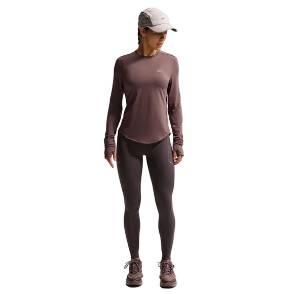 En person står med ansigtet fremad og har en Nike Swift UV langærmet løbetrøje til kvinder i farvekombinationen Tattoo/Reflective Silver på – en løbetrøje med indbygget UV-beskyttelse – kombineret med matchende leggings, rødbrune sneakers og en lysegrå Nike-kasket. Baggrunden er ensfarvet hvid, og personens hoved er let drejet mod højre.