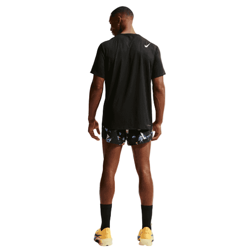 En mand står med ryggen til og er iført en sort Nike t-shirt, Nike Dri-FIT ADV 2" Brief-Lined Running Shorts til mænd i Black/Laser Orange med et mønstret design, sorte sokker og gule løbesko på en almindelig hvid baggrund.