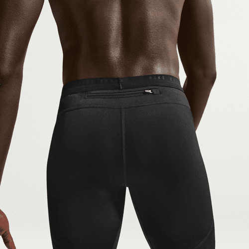 En person ses bagfra iført Nike Nk Df Stride Half Tight, Herre, Black/Reflective Silv, der fremhæver en lille vandret lynlåslomme på linningen. Billedet fokuserer på taljen og det øverste af benene mod en almindelig baggrund.