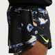 Nærbillede fra siden af en person iført Nike Dri-FIT ADV 2" Brief-Lined Running Shorts til mænd i Black/Laser Orange med et abstrakt blåt og orange diamantmønster, et gult Nike-logo og "DRI-FIT ADV" nær linningen.