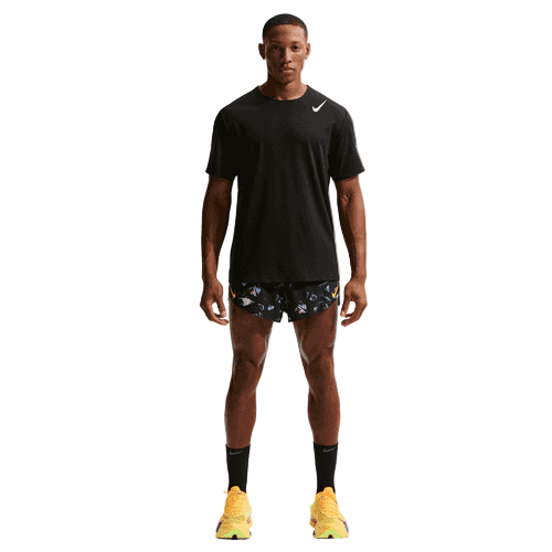 En mand kigger fremad mod en hvid baggrund iført en sort Nike t-shirt, Dri-FIT ADV 2" Brief-Lined Running Shorts Herre Black/Laser Orange, sorte knæstrømper og gule sportssko.
