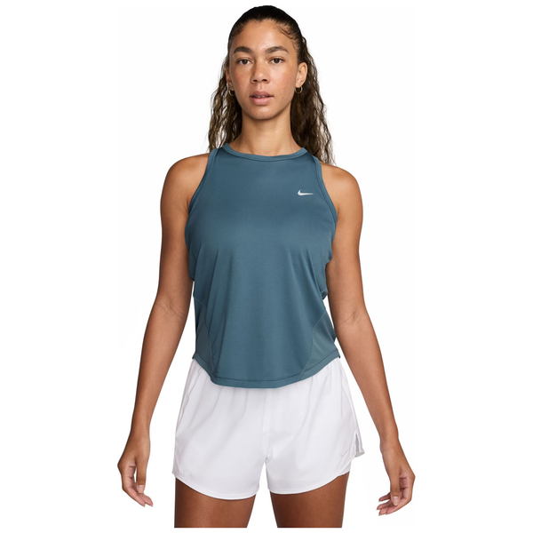 En kvinde iført en Nike Dri-FIT Running Tank Top til kvinder i Smokey Blue/Reflective Silver og hvide shorts står med front mod en almindelig hvid baggrund.