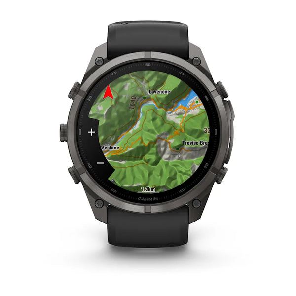 Et sort Garmin fenix 9 Pro InReach småur på 51 mm med en kulgrå DLC-titaniumramme og en sort, småstensgrå silikonerem viser et topografisk kort med terræn, højdekurver, veje, stednavne og en rød navigationspil på sin runde skærm.