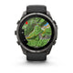 Et sort Garmin fenix 9 Pro InReach småur på 51 mm med en kulgrå DLC-titaniumramme og en sort, småstensgrå silikonerem viser et topografisk kort med terræn, højdekurver, veje, stednavne og en rød navigationspil på sin runde skærm.
