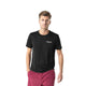 En mand med kort lysebrunt hår er iført en sort LiiteGuard Ground-Tech T-shirt, Herre, med et lille hvidt logo på brystet og rødbrune shorts. Han står på en almindelig hvid baggrund med den ene hånd i lommen.