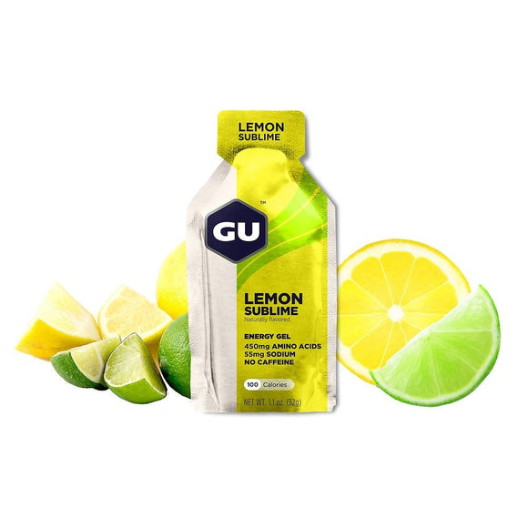 En GU Energy Gel, Lemon Sublime-pakke fra GU Energy står foran skiveskårne citroner og lime og fremhæver 450 mg aminosyrer, 55 mg natrium, ingen koffein og "energigel" - perfekt sportsernæring til din træning.