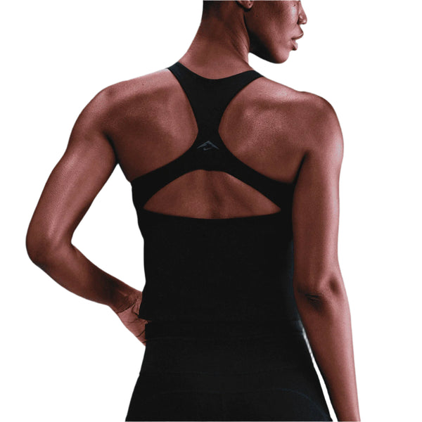 En kvinde iført en Nike Outdoor Bra Tank i Black/Summit White ses bagfra med venstre hånd hvilende på hoften mod en hvid baggrund.