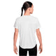 En person med en flettet frisure ses bagfra iført en Nike Dri-FIT kortærmet løbetop til kvinder i hvid/reflekterende sølv og sorte bukser på en hvid baggrund.
