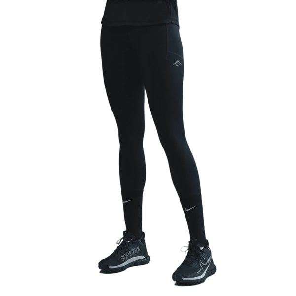 En person i Nike Trail 7/8 Tights, Dame, Black/Black står på en hvid baggrund, parret med sorte Nike-sokker og sorte Gore-Tex-atletiksko. Personens overkrop og hoved er ikke synlige.
