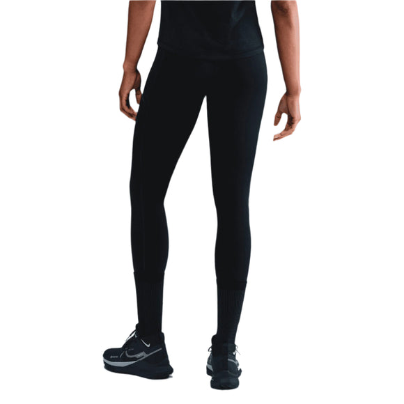 En person står med ryggen til og er iført en sort t-shirt, Nike Trail 7/8 Tights Dame Black/Black og sorte Nike-atletiksko med hvide såler og logoer. Baggrunden er almindelig hvid.