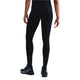 En person står med ryggen til og er iført en sort t-shirt, Nike Trail 7/8 Tights Dame Black/Black og sorte Nike-atletiksko med hvide såler og logoer. Baggrunden er almindelig hvid.
