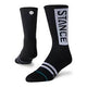Et par sorte Stance OG UL Crew unisex-strømper. På den ene står der "STANCE" med store hvide bogstaver, på den anden et lille cirkelformet logo. Begge har hvide og grå striber ved tæerne og er fugttransporterende.