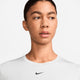 En kvinde med kort, mørkt hår bærer en hvid Nike Dri-Fit Short-Sleeve Top (Dame, White/Black), fremstillet af genbrugspolyester, og kigger til siden mod en almindelig lys baggrund.