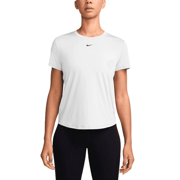 En kvinde står med front mod en hvid baggrund, klædt i sorte bukser og en Nike Dri-Fit Short-Sleeve Top (Dame) i hvid/sort, fremstillet af genanvendt polyester med et lille sort Nike-logo på brystet.