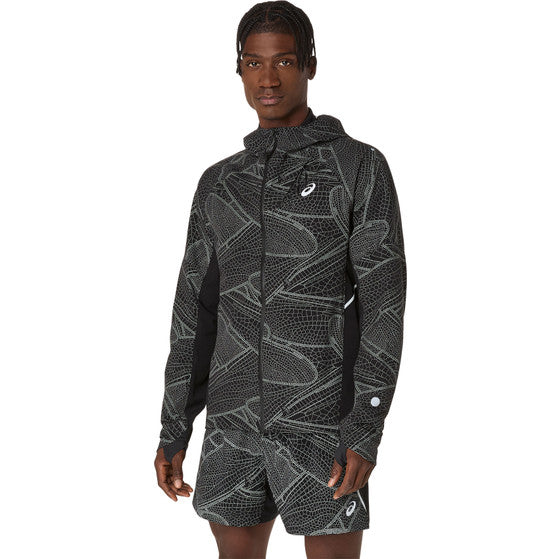 En person i en matchende sort og grå Limited Series Lite-Show Jacket, Herre fra Asics står med ansigtet fremad, den ene hånd ved siden af sig og den anden let løftet. Jakken har hætte, lynlås og ASICS refleks-teknologi for synlighed.
