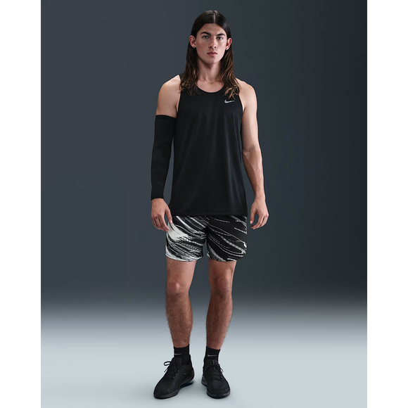 En person med langt hår er iført en sort ærmeløs tanktop, Nike Stride 7" Brief-Lined Running Shorts i Photon Dust/Reflective Silver, sorte sneakers og et sort ærme på venstre arm, og han står på en hvid baggrund.