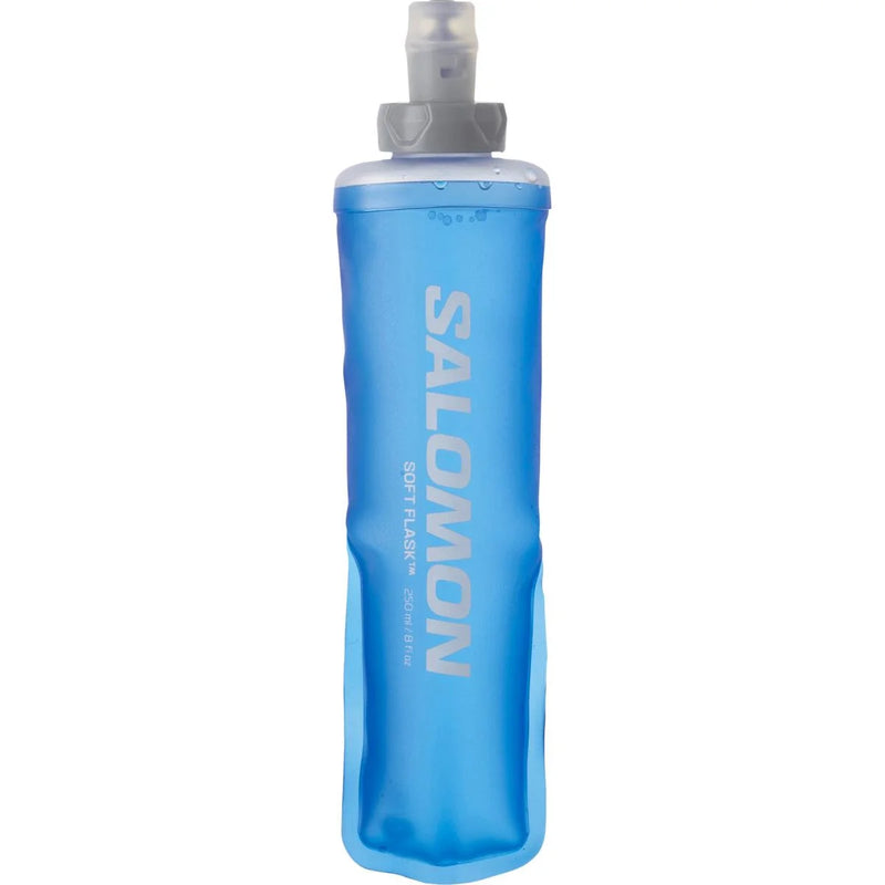 En klar blå Salomon Soft Flask 250 ml, Unisex, med grå hætte og dyse står oprejst. Den er lavet af fleksibelt materiale, og det hvide Salomon-logo og produktinfo er trykt lodret på siden.