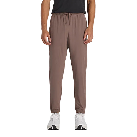 En person iført sort t-shirt, New Balance Athletics Run Jogger herre i Cortado med elastik i taljen og hvide sportssko står med front mod en almindelig hvid baggrund.