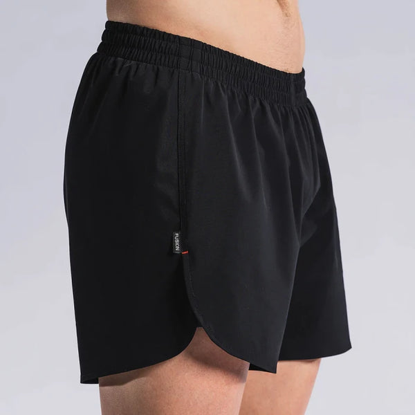 En person er iført Fusion Run Shorts, Herre, Black med elastisk linning, let buet kant og lille stofmærke i siden. Shortsene er lavet af svedtransporterende materiale. Baggrunden er ensfarvet og lys.