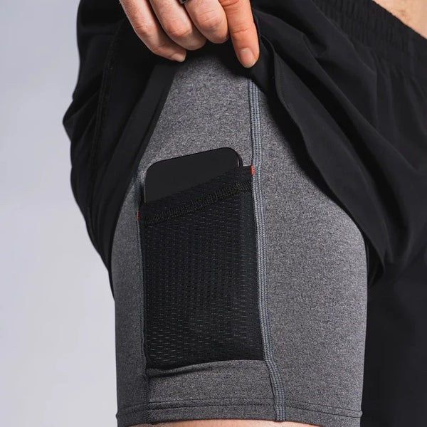 En person løfter Fusion Run Shorts, Herre, Black for at afsløre grå, svedtransporterende kompressionsshorts med en netlomme til en smartphone - perfekt til fans af løbeshorts.