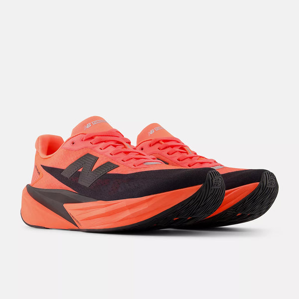 Et par New Balance FuelCell Rebel V5 dame løbesko i Urgent Red/Black/Silver Metallic med overdel i mesh, tyk sål og fedt N-logo vises på en almindelig hvid baggrund.