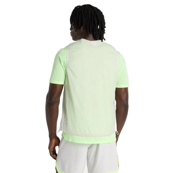 En person med kort, snoet hår kigger væk og er iført en lysegrøn kortærmet skjorte, New Balance Rc Vest Herre i grå og lyse shorts med neonfarvede detaljer på en almindelig hvid baggrund.