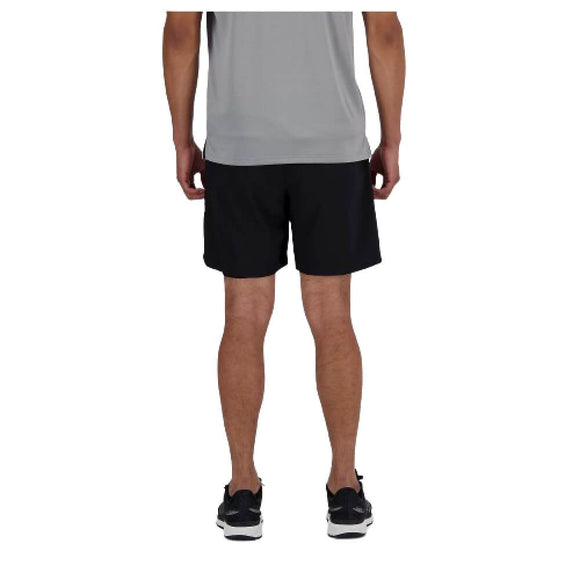 En person kigger væk fra kameraet iført en lysegrå T-shirt og New Balance AC Lined Shorts 7", Herre, Black. De har også sorte sportssko på, med en almindelig hvid baggrund.