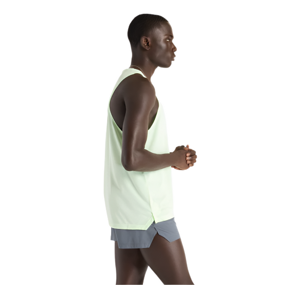 En person står i profil mod en hvid baggrund, iført New Balance Athletics Singlet, Herre, Melon Water og grå shorts med hænderne foldet foran.