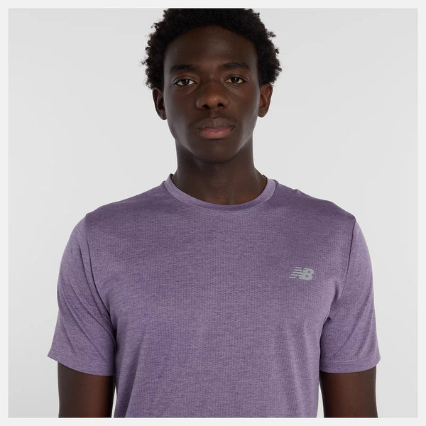 En mand er iført en New Balance Athletics T-shirt, Herre, i Candied Violet Heather og står med ansigtet vendt fremad med et neutralt udtryk mod en almindelig hvid baggrund.