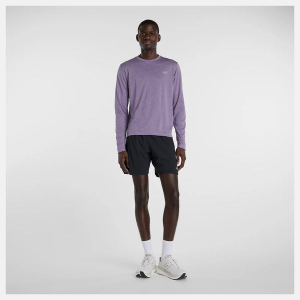 En mand står med front mod en almindelig hvid baggrund iført en New Balance Athletics Long Sleeve, Herre, i Candied Violet Heather, sorte shorts, hvide sokker og hvide løbesko.