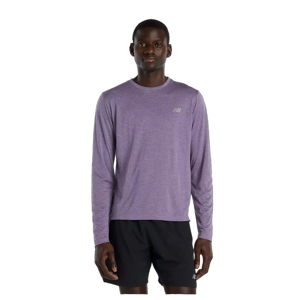 En person står og kigger fremad iført en New Balance Athletics Long Sleeve, Herre, Candied Violet Heather med et lille logo på brystet og sorte shorts. Baggrunden er almindelig hvid.