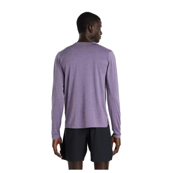 En person står med front mod kameraet iført en New Balance Athletics Long Sleeve til mænd i Candied Violet Heather og sorte shorts på en almindelig hvid baggrund.