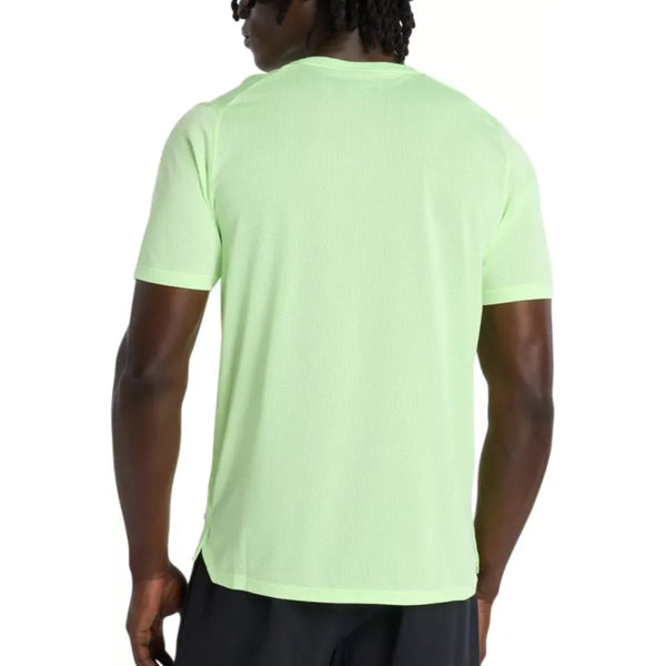 En person med mørk hud og skulderlangt hår ses bagfra iført en New Balance Athletics T-Shirt, Herre, Afterglow Heather, i lysegrøn og sorte shorts. T-shirten har ingen synlige logoer og er lavet af svedtransporterende materiale.