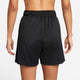 En person står med front mod kameraet i Nike Dri-FIT Fitness Mid-Rise 5" Unlined Shorts til kvinder i Black/Black/White/Reflective Silver med elastisk linning. Armene hviler i siden på en almindelig hvid baggrund.