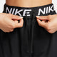 En person justerer den sorte løbegang på sine Nike Dri-FIT Fitness Mid-Rise 5" Shorts, der har en synlig linning med det store, hvide Nike-logo.