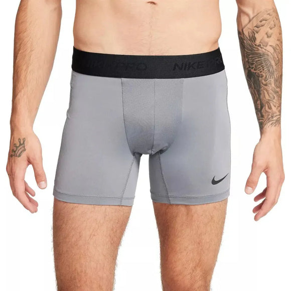 En person iført Nike Dri-Fit Brief Shorts til mænd i Smoke Grey/Black, med sort linning og lille Nike-logo på venstre ben. Tatoveringer er synlige på begge arme, og overkroppen vises fra skuldrene til midt på låret.