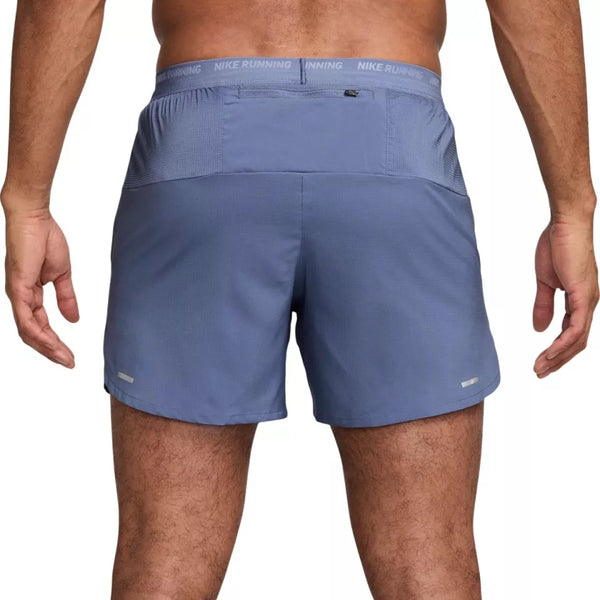 En person vises fra taljen og ned iført Nike Dri-FIT 5" Stride Running Shorts til mænd i World Indigo/Black/Reflective Silv, med ryggen og benene synlige.