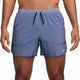 En mand i bar overkrop er iført blå Nike Dri-FIT 5" Stride Running Shorts (World Indigo/Black/Reflective Silv) med sort løbegang og elastisk linning med NIKE RUNNING påtrykt. Et lille Nike-logo er synligt på venstre ben.