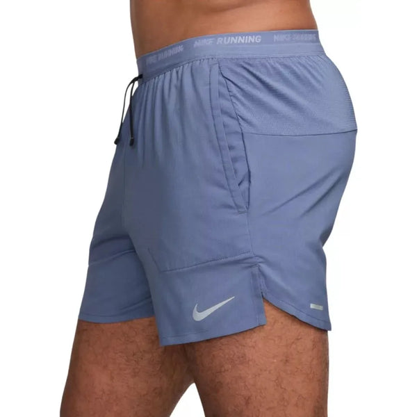 Et sidebillede viser en person iført Nike Dri-FIT 5" Stride Running Shorts, Herre, i World Indigo/Black/Reflective Silv. NIKE RUNNING-linningen og swoosh-logoet er synlige på midtersektionen og låret.