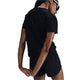 En kvinde i sorte Nike Dri-FIT-atletikshorts og en Dri-FIT Short-Sleeve Running Top, Dame, Black/Reflective Silv står med ryggen til kameraet, hænderne foldet bag sig, iført solbriller og kigger sig over højre skulder.