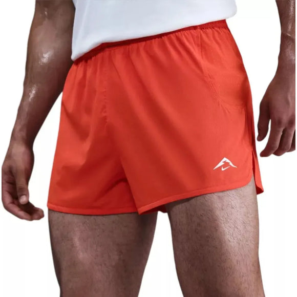 En person iført lyse Picante Red/Black Nike Trailwind 3" Shorts med Dri-FIT-teknologi og en hvid skjorte, vist fra taljen til midt på låret. Shortsene har et diskret hvidt logo, der er ideelt til trailløb. Personens hud glitrer af sved.