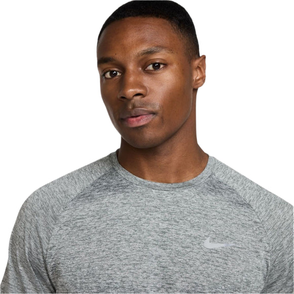 En mand bærer Nike Stride ADV Short-Sleeve Running Top, Herre, i Smoke Grey/Htr/Reflective Silver mod en almindelig hvid baggrund. Denne løbetrøje mænd kombinerer stil med Dri-FIT ADV-ydelse.