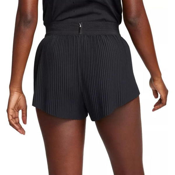 En kvinde ses bagfra iført Nike Aeroswift 3" Shorts, Dame, i sort/hvid, stående med afslappede arme langs siden mod en ensfarvet baggrund.