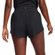 En kvinde ses bagfra iført Nike Aeroswift 3" Shorts, Dame, i sort/hvid, stående med afslappede arme langs siden mod en ensfarvet baggrund.